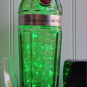 May include: A green glass bottle with a label that reads "Tanqueray No. Ten" and a red cap. The bottle is filled with green fairy lights.