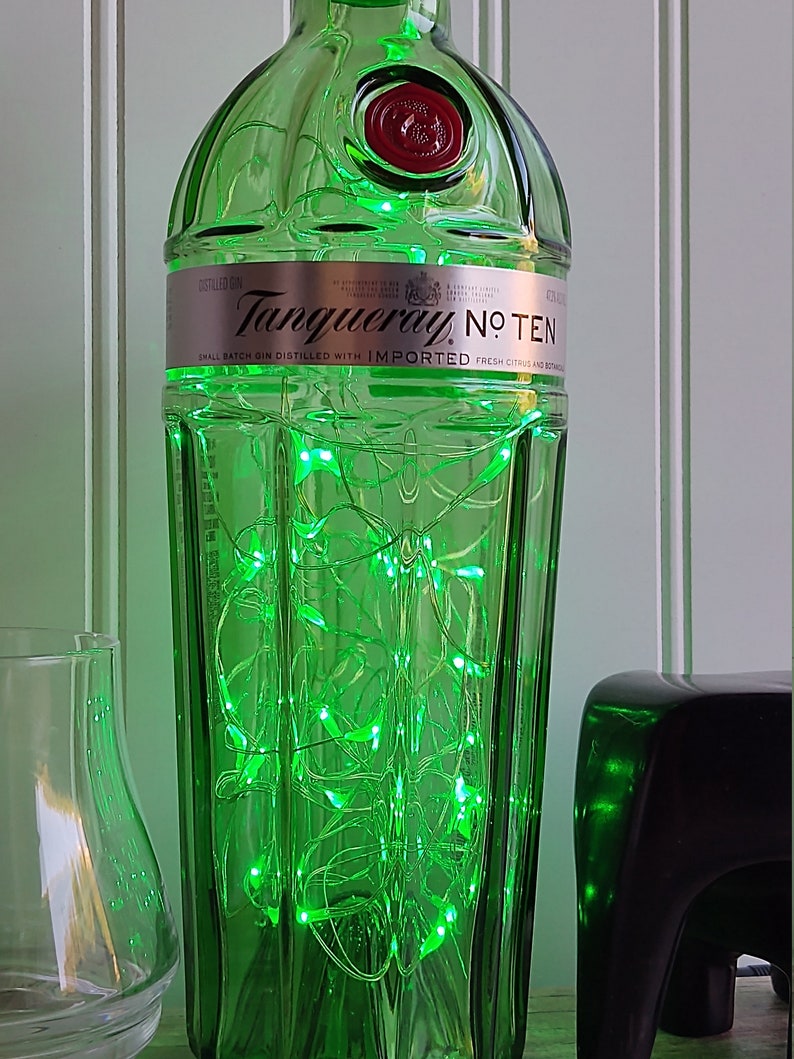 May include: A green glass bottle with a label that reads "Tanqueray No. Ten" and a red cap. The bottle is filled with green fairy lights.