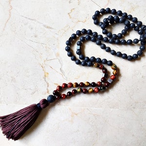 May include: A black lava stone mala necklace with a tassel. The mala is made with red, gold, and brown tiger's eye beads.