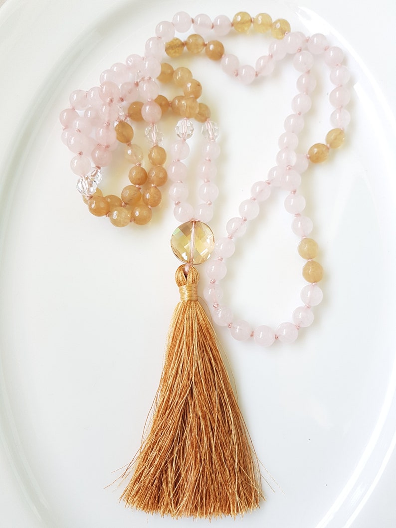 May include: A mala or prayer beads necklace with pink and brown beads and a gold tassel. The beads are strung on a clear cord.