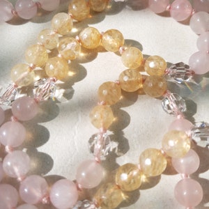 May include: A long necklace with alternating beads of light pink and yellow-gold. The beads are strung on a thin pink cord.