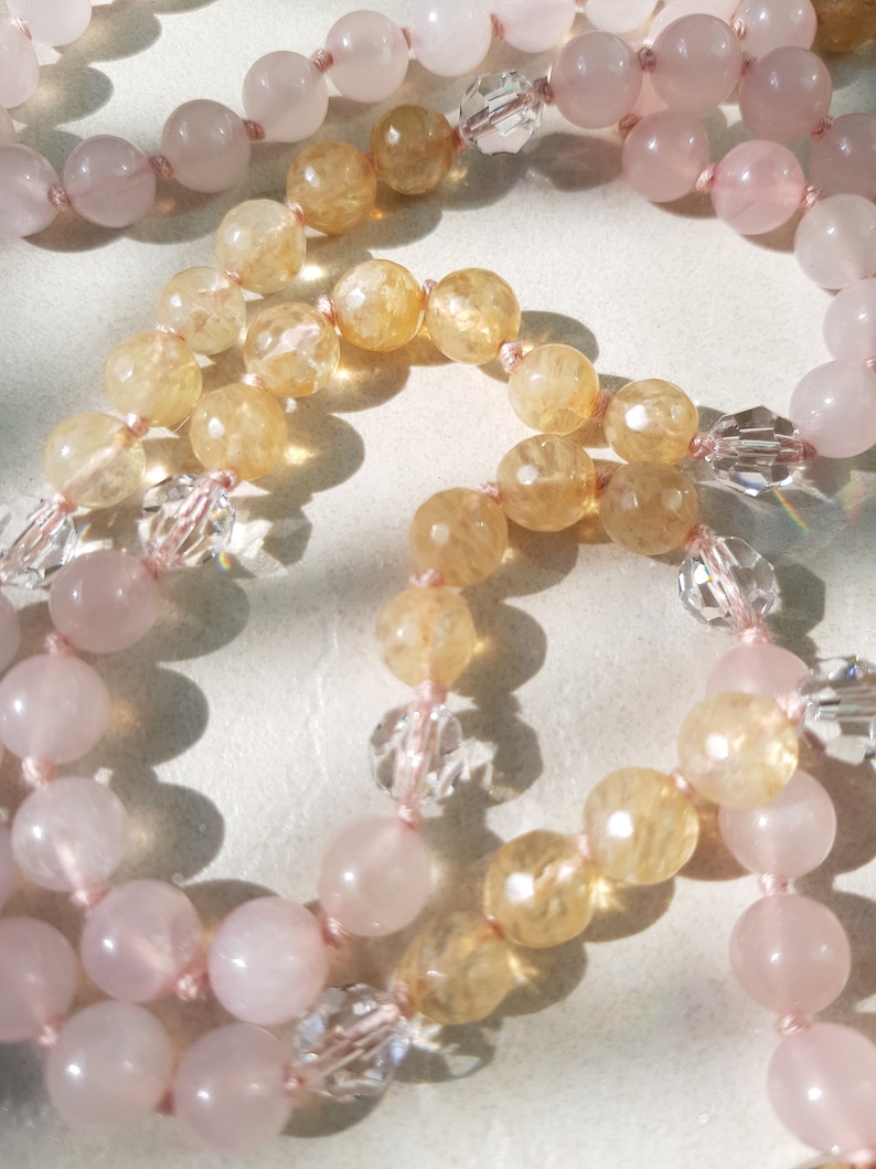 May include: A long necklace with alternating beads of light pink and yellow-gold. The beads are strung on a thin pink cord.