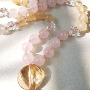 May include: A long strand of beads made with pink and yellow gemstones. The beads are strung on a thin cord and have a gold tassel at the end.