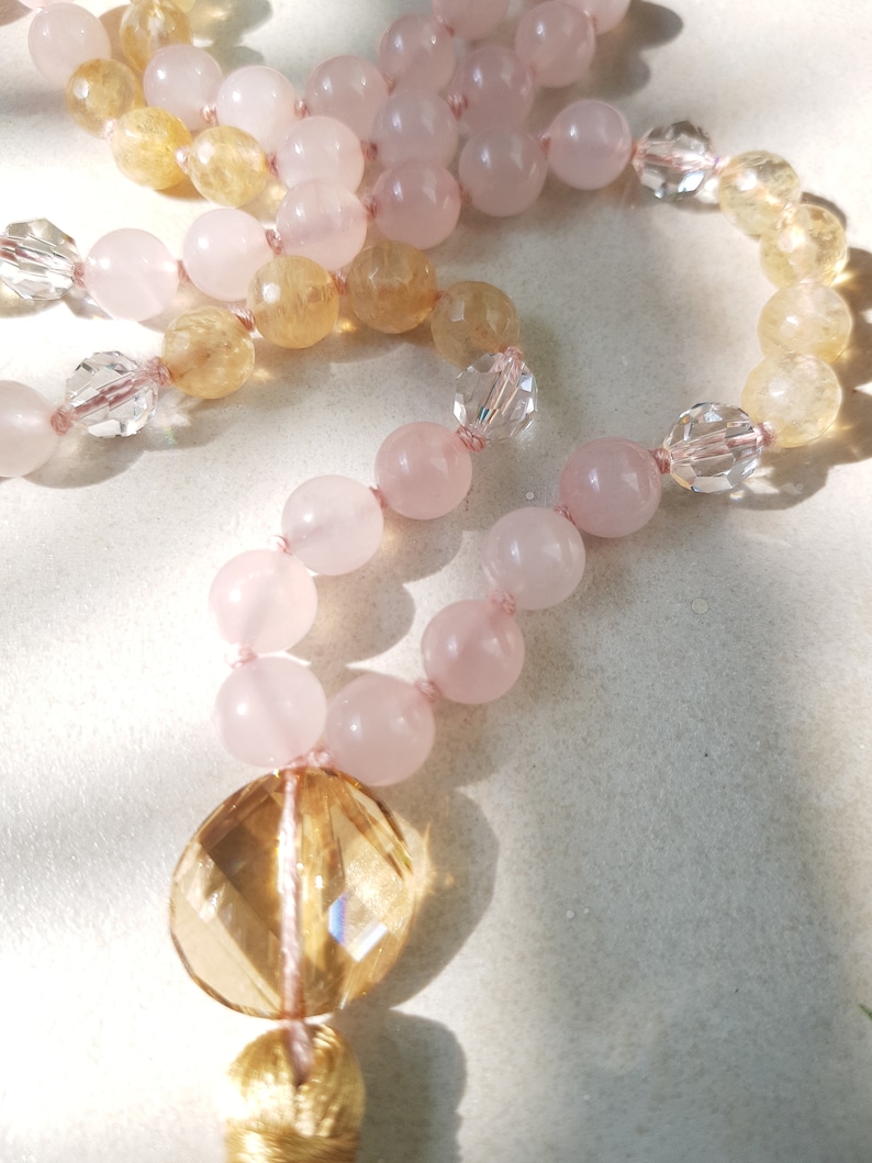 May include: A long strand of beads made with pink and yellow gemstones. The beads are strung on a thin cord and have a gold tassel at the end.