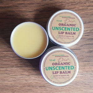 May include: Two 15 ml tins of Oris Organic Unscented Lip Balm. The tins are handmade and suitable for sensitive skin. The tins are labelled with the brand name, product name, and size. The tins are on a wooden surface.