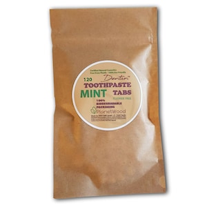 May include: A brown paper bag with a white circle label that says "Dentin Toothpaste Tabs Mint 120 Fluoride Free 100% Biodegradable Packaging Planet Wood Made by DENTTABS Germany - D-1347 Berlin"