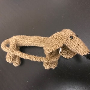 May include: A crocheted dachshund toy with brown fur, black eyes, and a black nose.