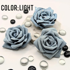 May include: Three light blue denim fabric rose flowers with glitter accents. The flowers are arranged on a white surface with decorative glass beads. The text "COLOR; LIGHT" is in the upper left corner.