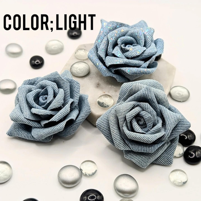 May include: Three light blue denim fabric rose flowers with glitter accents. The flowers are arranged on a white surface with decorative glass beads. The text "COLOR; LIGHT" is in the upper left corner.