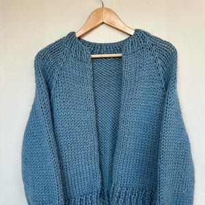 Può includere: Un cardigan di maglia blu chiaro con una vestibilità rilassata e maniche lunghe.