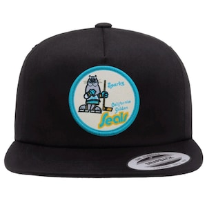 May include: Black and teal baseball cap with a circular patch featuring a cartoon seal wearing a hockey jersey and holding a hockey stick. The patch says "Sparky California Golden Seals".