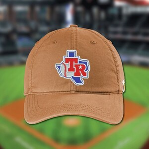 May include: A tan baseball cap featuring an embroidered patch of the state of Texas in blue with a white outline. The patch includes a white baseball graphic and the red letters TR with a white star inside the letter R on the front panel.