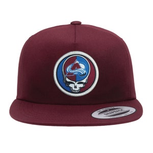 May include: A maroon baseball cap with a circular patch featuring a skull and crossbones design with a blue and red Colorado Avalanche logo.