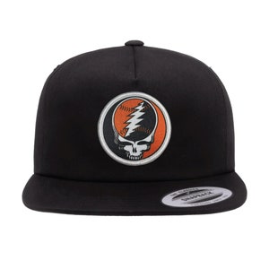 May include: Black baseball cap with a circular patch featuring a skull and lightning bolt design in orange and white.