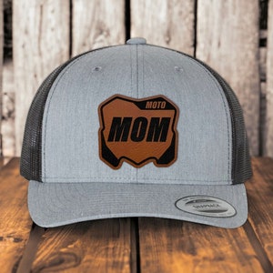 May include: Gray and black trucker hat with a brown leather patch that says "MOTO MOM" in black letters.