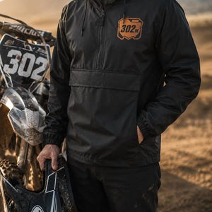 Rider wearing a custom motocross windbreaker with personalized name and number leather patch at an outdoor dirt bike track.