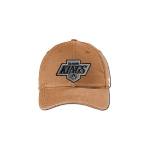 K&ouml;nnte beinhalten: Eine braune Baseballkappe aus Baumwolle mit einem gestickten Los Angeles Kings Logo in Schwarz und Silber.