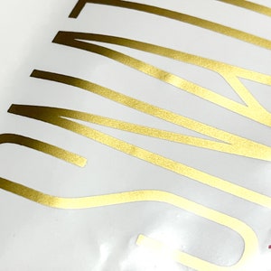 May include: Close-up of a gold foil sticker with the word "SUMMER" written in a stylized font.