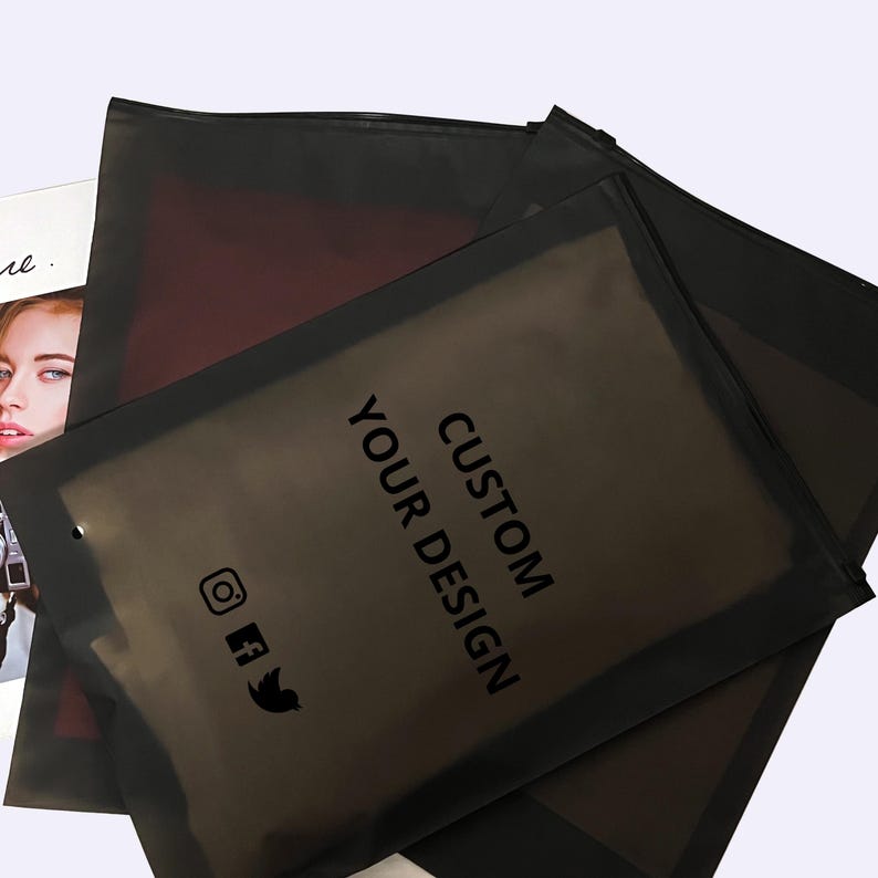 Peut inclure: Plusieurs sacs d'emballage noirs personnalis&eacute;s sont empil&eacute;s, avec les mots "CUSTOM YOUR DESIGN" imprim&eacute;s en noir. Des ic&ocirc;nes de m&eacute;dias sociaux sont &eacute;galement visibles. Un magazine avec le visage d'une femme est partiellement visible en arri&egrave;re-plan.
