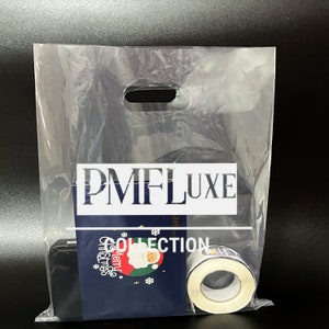 May include: A clear plastic shopping bag with a white handle. The bag has a white label with the text "PMFLUXE COLLECTION" printed on it. The bag contains a black box with a Christmas themed sticker and a roll of white tape.