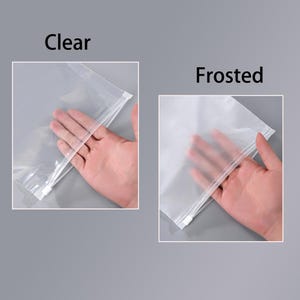 Op de afbeelding: Twee plastic opbergzakken met ritssluiting. De linkerzak is gelabeld als Clear en is transparant, terwijl de rechterzak is gelabeld als Frosted en een semi-transparante, matte afwerking heeft met een witte ritssluiting.