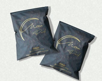 Peut inclure: Deux sacs d'emballage noirs avec des détails dorés. Les sacs ont une fermeture éclair et présentent le texte "Mona Pack" en script doré, ainsi que des icônes de médias sociaux et une adresse de site Web. Les sacs sont sur fond blanc.
