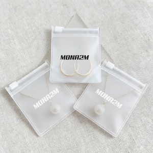 May include: Three clear plastic zip bags containing jewelry. One bag holds gold hoop earrings, and the other two contain necklaces with a single pearl pendant. Each bag has the text "MONA2M" printed on it.