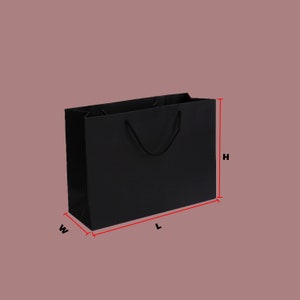Puede incluir: Una bolsa de papel negra con un asa de cuerda negra. La bolsa est&aacute; etiquetada con las letras "W", "L" y "H" para indicar ancho, largo y alto.