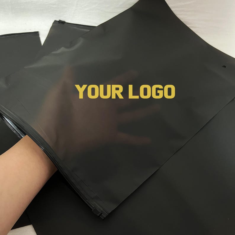 Peut inclure: Sacs postaux noirs avec l'inscription dor&eacute;e "YOUR LOGO". Les sacs sont dot&eacute;s d'une fermeture &eacute;clair et sont pr&eacute;sent&eacute;s empil&eacute;s. Les sacs sont fabriqu&eacute;s dans un mat&eacute;riau durable.