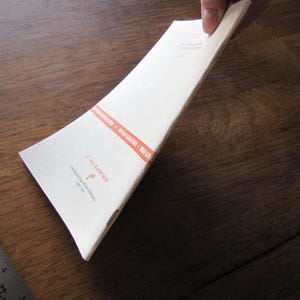 May include: A white paper book with the text "A TALE BLAZER BOOK" and "WRAPAROUND" in orange. The book is held by a person's hand. The book is on a wooden surface.