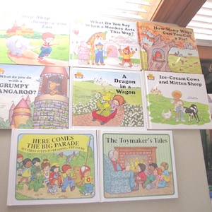 May include: A collection of children's books with colorful illustrations. Titles include "Hop, Skip, Jump-a-roo Zoo", "What Do You Say When a Monkey Acts This Way?", and "Here Comes the Big Parade". The books are stacked on a shelf.