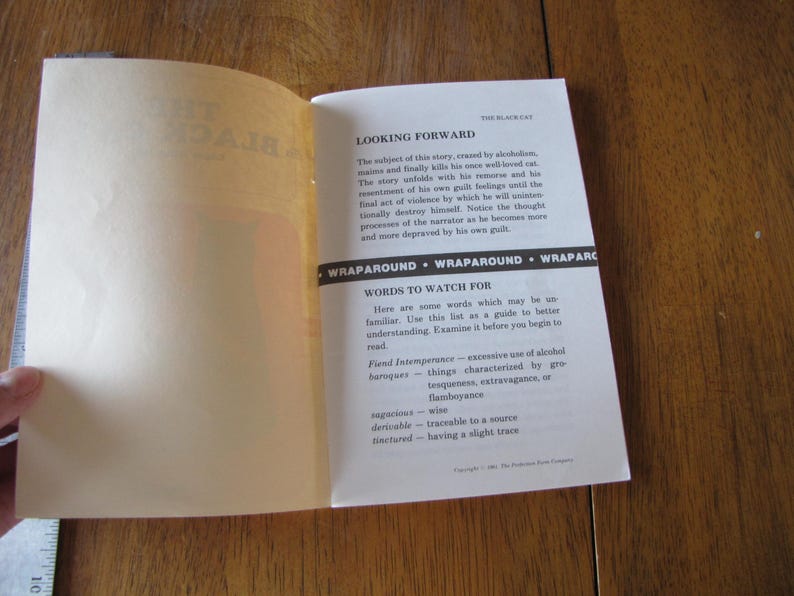 May include: Open book with text from "The Black Cat" story. The pages are off-white with black text. The text includes "Looking Forward" and "Words to Watch For". The book is open on a wooden surface.