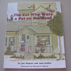May include: The cover of a children's book titled "The Cat Who Wore a Pot on Her Head". The cover features a cartoon illustration of a house with a cat wearing a pot on its head.