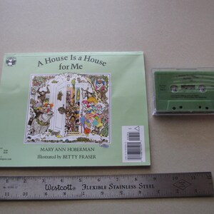 May include: A children's book titled "A House Is a House for Me" with a colorful illustration and a green cassette tape. A flexible stainless steel ruler is also present. The book cover features the author's and illustrator's names.