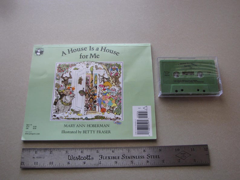 May include: A children's book titled "A House Is a House for Me" with a colorful illustration and a green cassette tape. A flexible stainless steel ruler is also present. The book cover features the author's and illustrator's names.