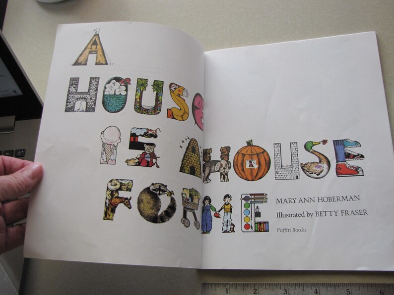 May include: Open book with the title "A House Is Home" in colorful, illustrated letters. The book's text is by Mary Ann Hoberman and illustrated by Betty Fraser. The letters are decorated with images of a tent, house, ice cream cone, and more.