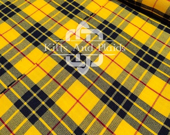 Op de afbeelding: Gele, zwarte en rode tartan stof met de tekst "Kilts And Plaids" in het midden.