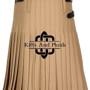 May include: A tan kilt with black buckles and pleats. The kilt has a black logo with the text "Kilts And Plaids" on it.