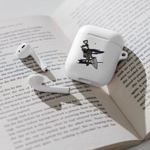 Op de afbeelding: Witte draadloze oordopjes in een beschermend hoesje met een afbeelding van een skelet dat een schop vasthoudt. Het hoesje heeft een blauw en zwart ontwerp. De oordopjes liggen op een boek met tekst over een brief.