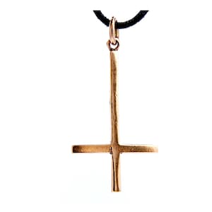 May include: A gold-colored pendant featuring an inverted cross design, suspended from a black cord. The pendant has a vertical bar intersected by a horizontal bar, creating the inverted cross shape. The background is plain white.