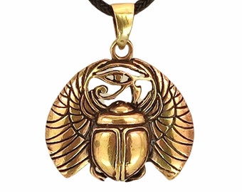 May include: A gold-toned metal pendant featuring a winged scarab beetle with an Eye of Horus symbol above it. The pendant is suspended from a dark brown braided cord. The design is symmetrical with detailed engravings on the wings and body.