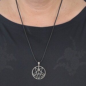 May include: A silver pendant necklace with a black cord. The pendant is a circle with a pentagram inside. The pentagram has a cross in the center.