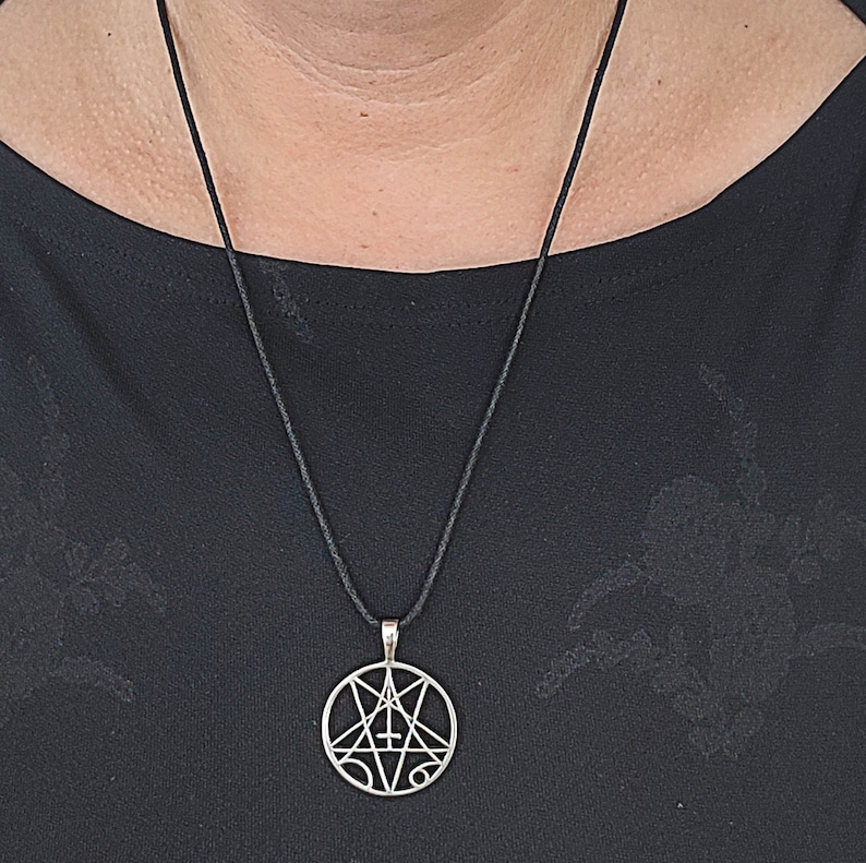 May include: A silver pendant necklace with a black cord. The pendant is a circle with a pentagram inside. The pentagram has a cross in the center.