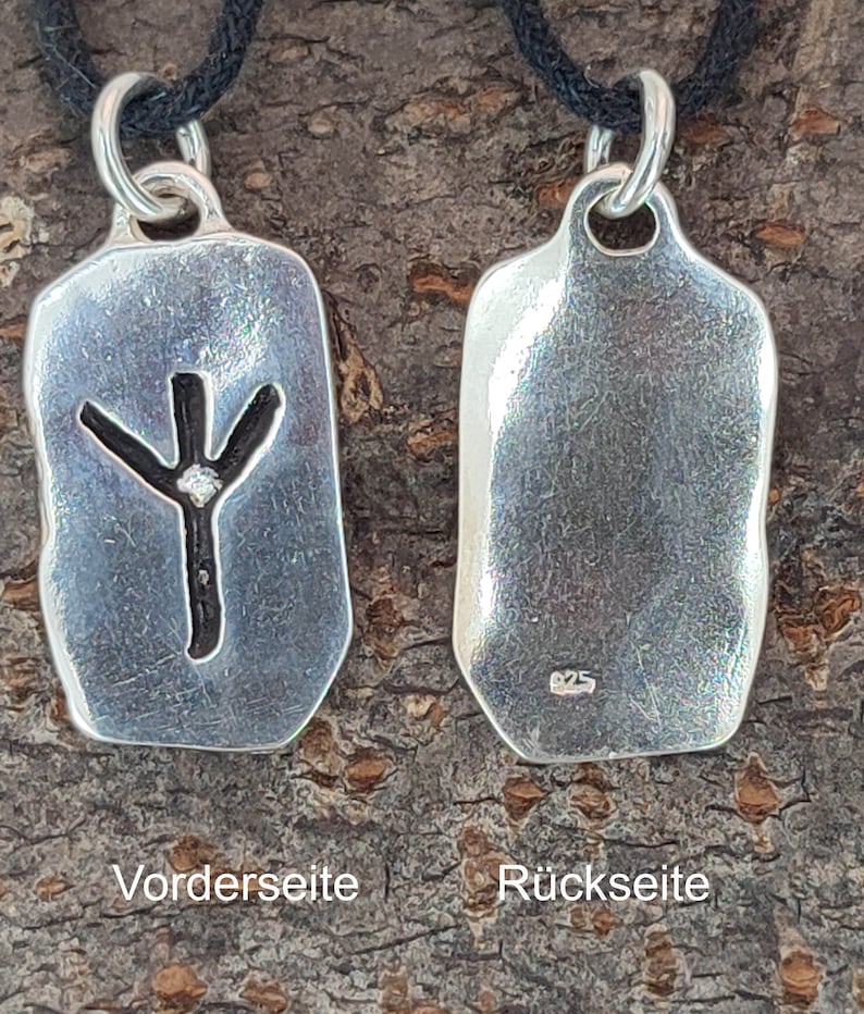 Puede incluir: Colgante de plata con un s&iacute;mbolo de runa en la parte delantera y un sello 925 en la parte posterior. El colgante est&aacute; en un cord&oacute;n negro.