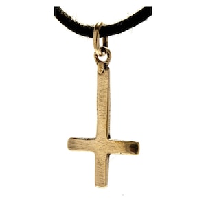 May include: A gold-toned metal pendant in the shape of an inverted cross, featuring a brushed texture on its surface. The pendant is suspended from a simple, thick black cord that passes through a small metal jump ring at the top of the cross.