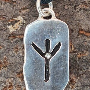 Puede incluir: Colgante de plata con una runa Yggdrasil negra y un peque&ntilde;o diamante en el centro. El colgante est&aacute; en un cord&oacute;n negro.