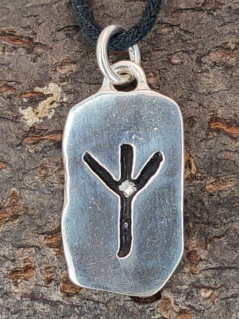 Puede incluir: Colgante de plata con una runa Yggdrasil negra y un peque&ntilde;o diamante en el centro. El colgante est&aacute; en un cord&oacute;n negro.