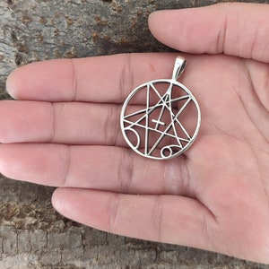 May include: Silver pendant with a circular design featuring a five-pointed star with a cross inside. The star is surrounded by a circle with lines and symbols.