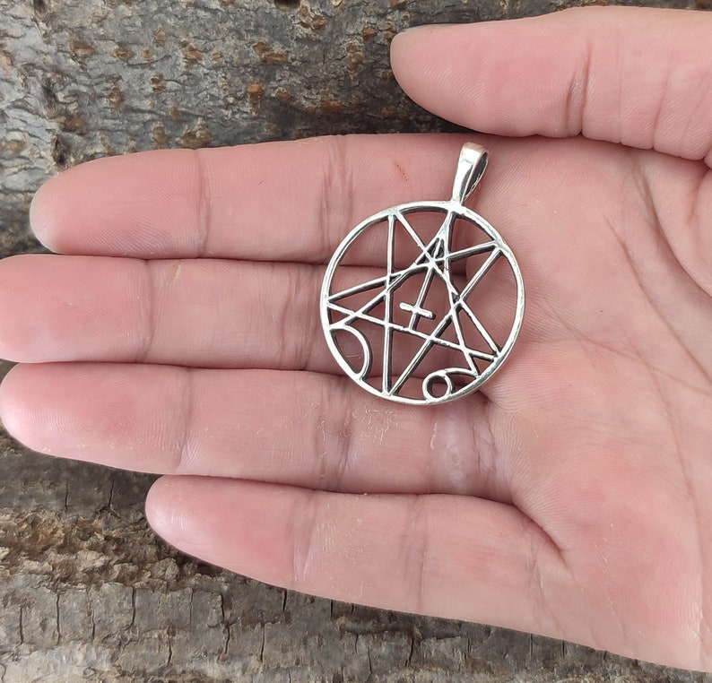 May include: Silver pendant with a circular design featuring a five-pointed star with a cross inside. The star is surrounded by a circle with lines and symbols.
