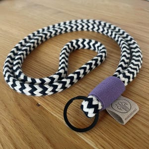 Könnte beinhalten: Schwarz-weißes Lanyard mit Chevron-Muster, einem violetten Stoffakzent und einem schwarzen Metallschlüsselring. Das Lanyard hat ein kleines braunes Leder-Etikett mit dem Text "#WOODCREEKNJ".